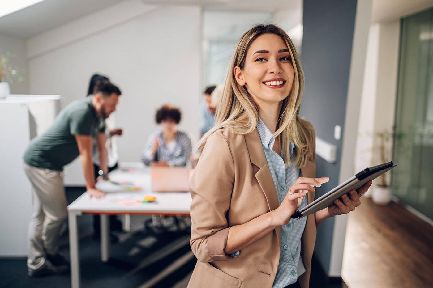 Smiling confident business leader looking at camera and standing in an office at team meeting. Portrait of confident businesswoman with colleagues in boardroom. Using digital tablet during a meeting.